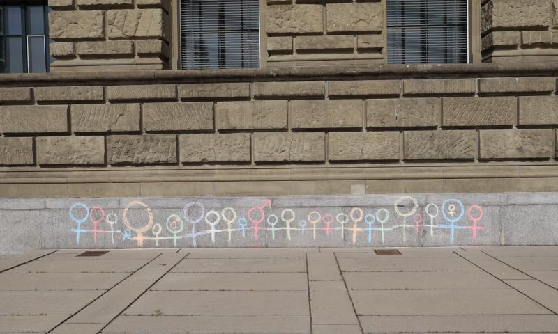 Brick exterior wall of building with multi-coloured chalk drawings of female and male symbols.